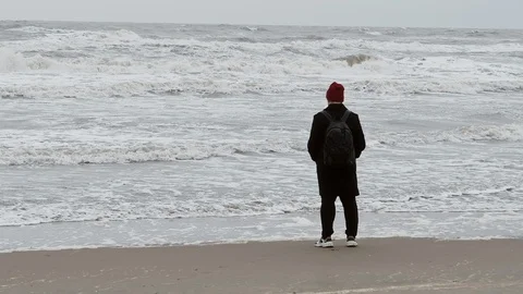 Yang hipster man in red hat step back from the waves on the beach in autumn 스톡 동영상 119556210