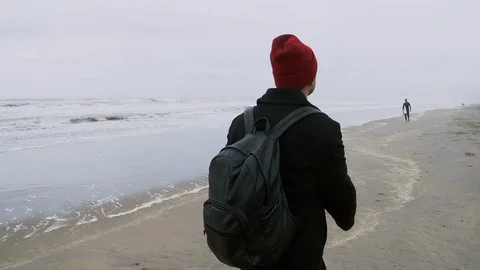 Yang man in red hat is walking alone across the beach in autumn. Vidéo 119556260