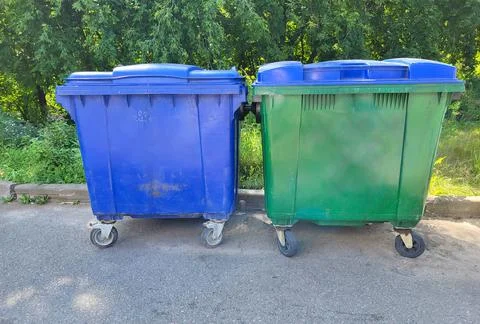 In the yard, two garbage containers stand against the backdrop of green sum.. Stock Photos