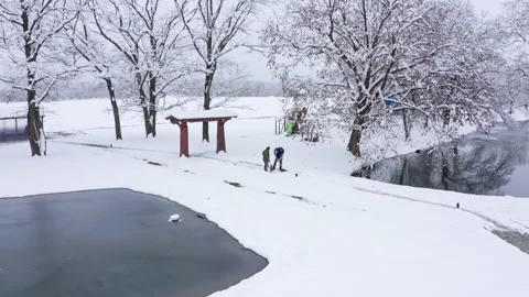 Yardmen clean snowy park path with shovels near lake Stock Footage 146678030