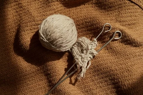 Yarn sits next to knitting needles on a textured brown fabric. The scene shows a Видео 336464817