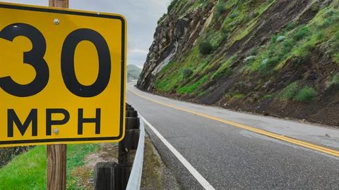 Yellow 30 MPH speed limit sign on a winding mountain road Stock Photos