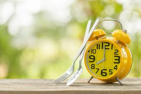 Yellow alarm clock, Fork, and spoon on wooden table with green outdoor natu.. Stock Photos