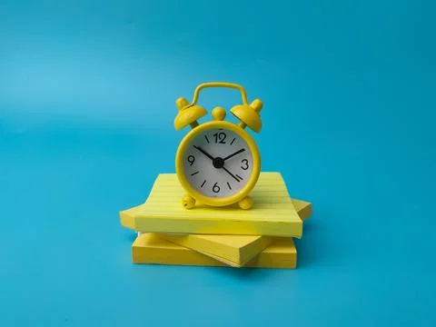 A yellow alarm clock sits on a stack of yellow sticky notes over a plain bl.. Stock Photos