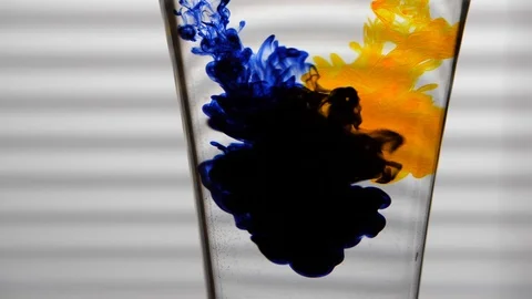 Yellow and Blue Dyes Dissolving in Glass of Water on White Background Video stock 104618393