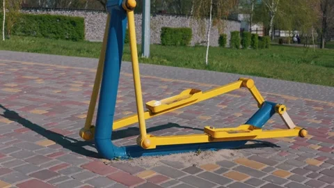 Yellow and Blue Elliptical Trainer Stands on a Stone Paved Path in a Public Park Video stock 333824873