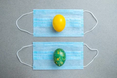 Yellow and green easter eggs lie on blue medical masks on a gray background. Stock Photos
