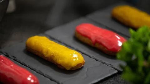 Yellow and pink glaze eclair on stone plates. Modern desserts and cakes Stock Photos