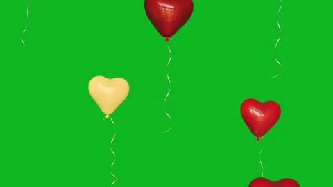 Yellow and red heart shaped helium balloons floating slowly upwards on green  Video stock 343096092