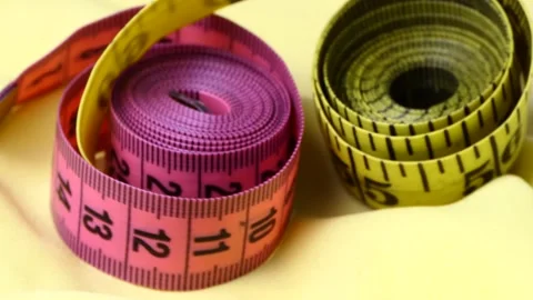 Yellow and red measuring tape rotating on a yellow fabric background Stock Footage 248367342