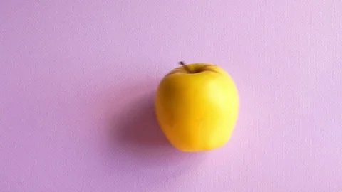 The yellow apple is rolling on the purple table and stay Stock Footage 112265752