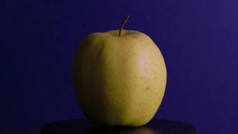 A yellow apple rotates around its axis on a blue background Stock Footage 330687235