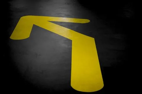Yellow arrow on a dark asphalt surface, pointing towards the upper left cor.. Stock Photos