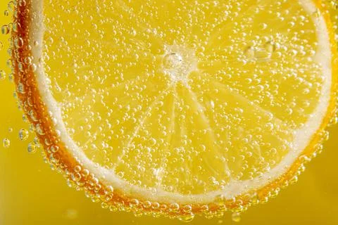 Yellow background with lemon slice with bubbles, close-up Stock Photos