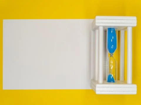 On a yellow background, a white leaf and an hourglass are the concept of the  Stock Photos