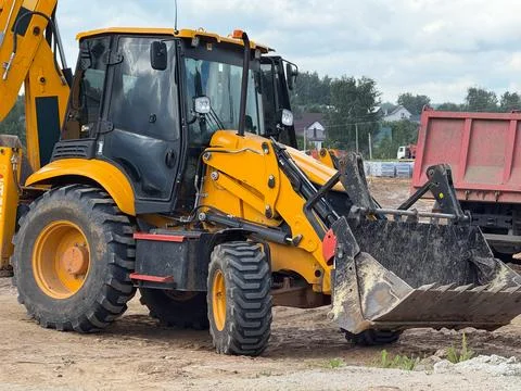 Yellow backhoe loader on a construction site with a red truck and banner spac Stock Photos