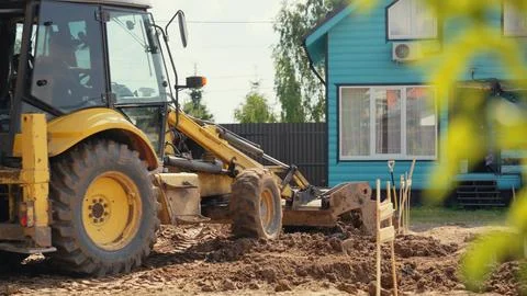Yellow backhoe loader digging ground near residential house Stock Photos