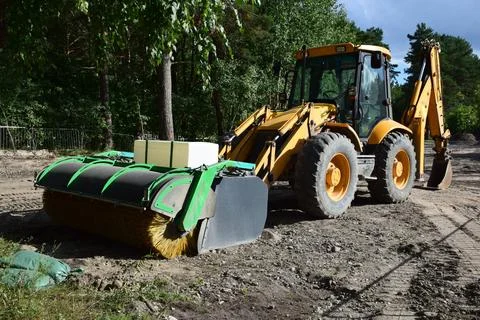 Yellow backhoe loader with front sweeper attachment on construction site Foto stock