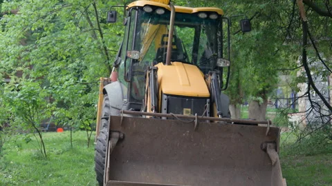 Yellow Backhoe Loader Parked Among Green Trees in Urban Yard | Front Bucket Stock Footage 335092312