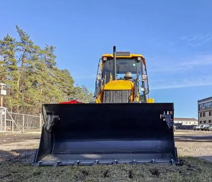 Yellow backhoe loader parked on construction site under bright blue sky wit.. Fotos Stock