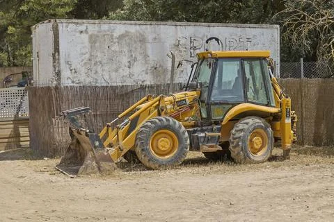 Yellow backhoe loader parked on construction site in daylight Stock Photos