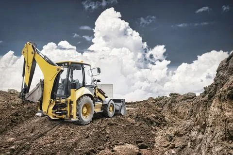 A yellow backhoe loader works at a construction site, digging into the ground Photos