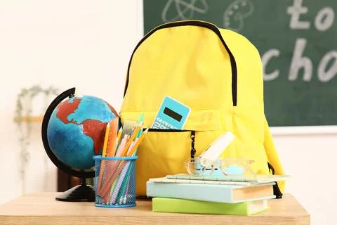 Yellow backpack with school supplies, globe, and books on a wooden desk in a  Stock Photos