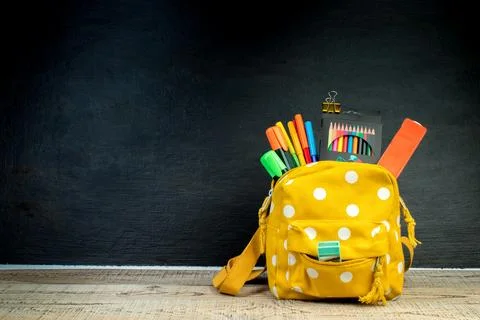 Yellow backpack with white polka dots with different colorful stationery on.. Stock Photos
