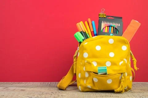Yellow backpack with white polka dots with different colorful stationery on.. Stock Photos