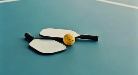Yellow Ball and Two Plain Pickleball Paddles on Smooth Blue Surface Stock Footage 317662182