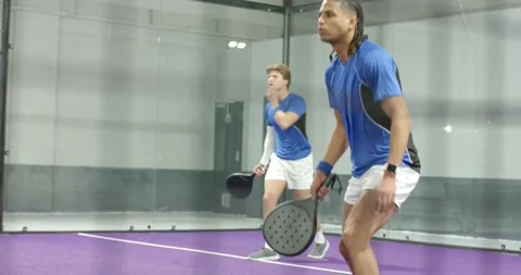 Yellow ball arcing toward diverse male padel duo, returning ball while training Stock Footage 340009288