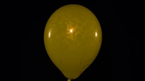 The yellow balloon bursts and releases sparkles and confetti into the aie, slow Stock Footage