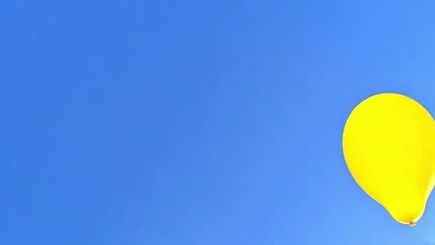 Yellow balloon drifting across clear blue sky with copy space Stock Footage 323975964
