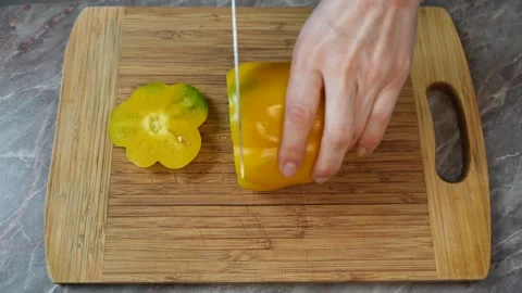 A yellow bell pepper is being cut with a kitchen knife Video stock 303573851
