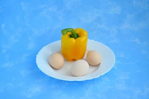 Yellow Bell Pepper with Three Eggs on White Plate and Blue Background Stock Photos