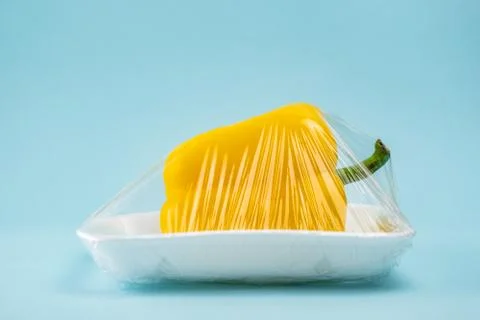 Yellow bell pepper wrapped in plastic clingfilm in blue background Stock Photos