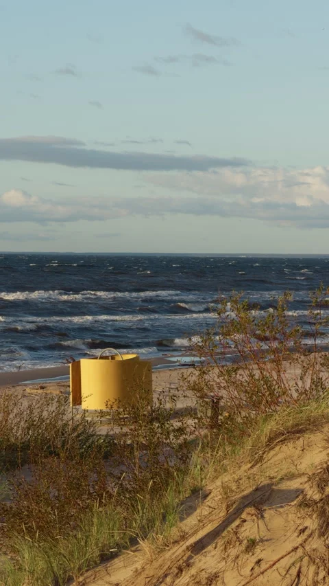 Yellow bin on windy sandy beach with ocean waves, dune grass, and soft cloudy Stock Footage 346558500