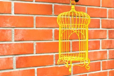 Yellow birdcage on brick wall background. Stock Photos