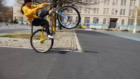 Yellow BMX Biker Kid Doing Wheelies In Public Park Stock Footage 128086029