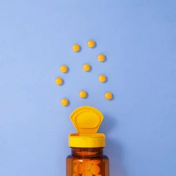 Yellow bottle container with medication tablets on blue background. Concept o Foto stock