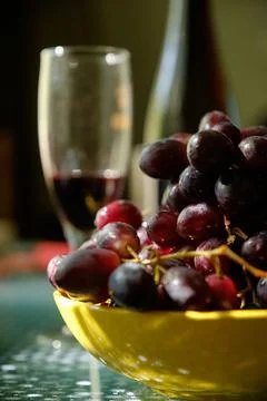 A Yellow bowl of ruby-red grapes, with a wine glass and bottle in the backg.. Stockfoto's