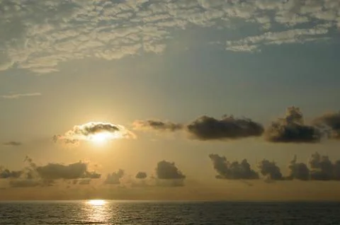 The yellow bright sun is covered by a cloud over the ocean. Stock Photos