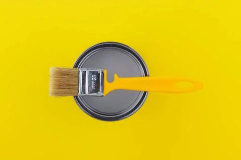 Yellow brush on an open can with gray paint on a yellow background close-u... Stockfoto's