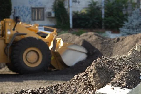 Yellow bucket loader out of focus pours sand on construction site Stock Photos