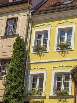 Yellow building with white window frames and flower boxes, next to it a high Stock Photos