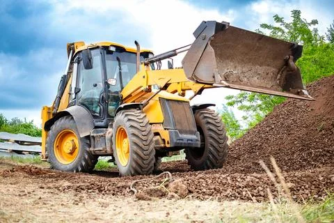 A yellow bulldozer or a loader is actively digging dirt in a field, moving an Stock-Fotos