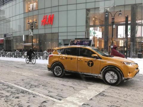 Yellow cab and two bike riders in front of H&M in midtown Manhattan on a snow Stock Photos