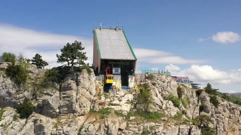 A yellow cabin of cableway going by cable along the rocky sheer wall of mount Stock Footage 165452991