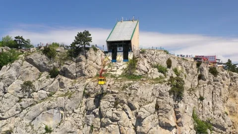 A yellow cabin of cableway going by cable along the rocky sheer wall of mount Stock Footage 165452995