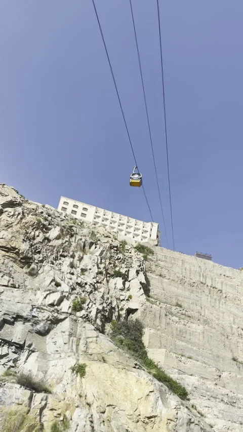 Yellow Cable Car Ascends Steep Rocky Cliff Face Under Blue Sky Vídeo Stock 320819764